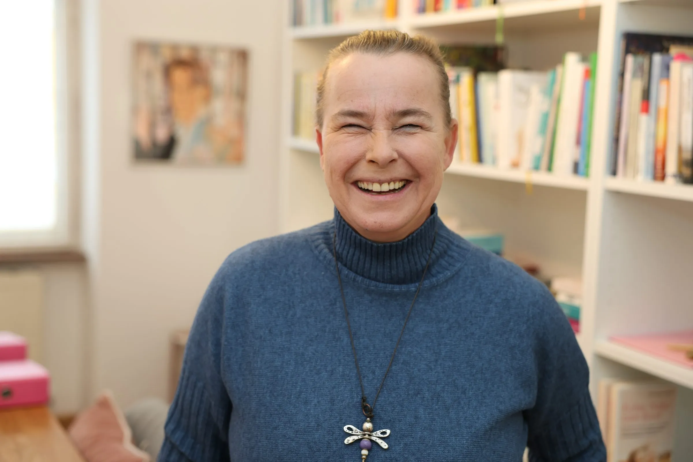 Porträt von Verena Broschek-Fellner, lachend vor dem Bücherregal