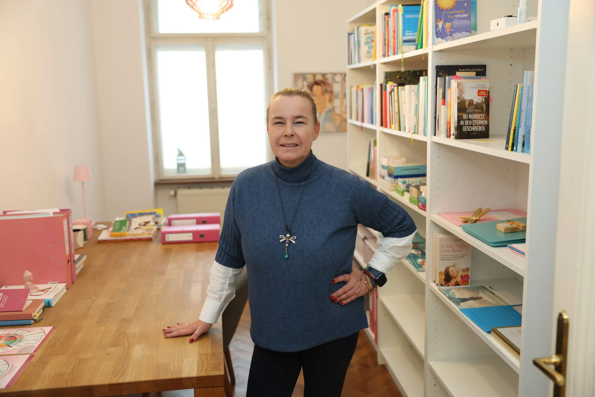 Verena Broschek-Fellner steht im Arbeitsraum des Glücksraums am Bücherregal